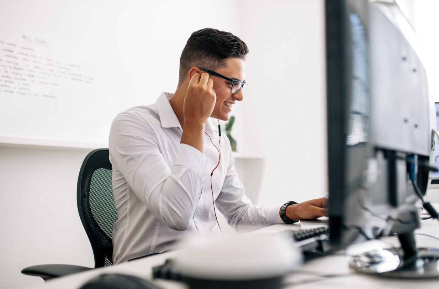 Lächelnder Mann setzt Kopfhörer auf, die an einen Computer angeschlossen sind.